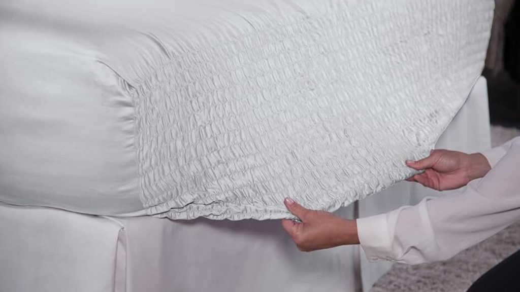A person neatly drapes a white sheet made with microfiber bedding materials
