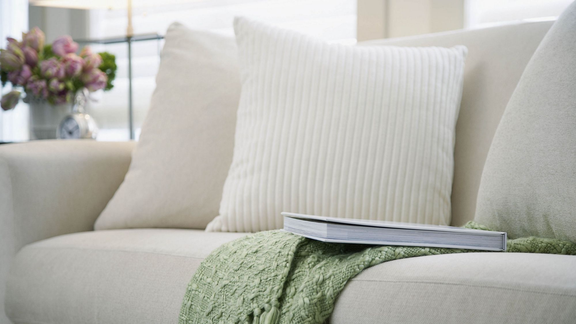 A white couch with a green blanket and a book in a living room